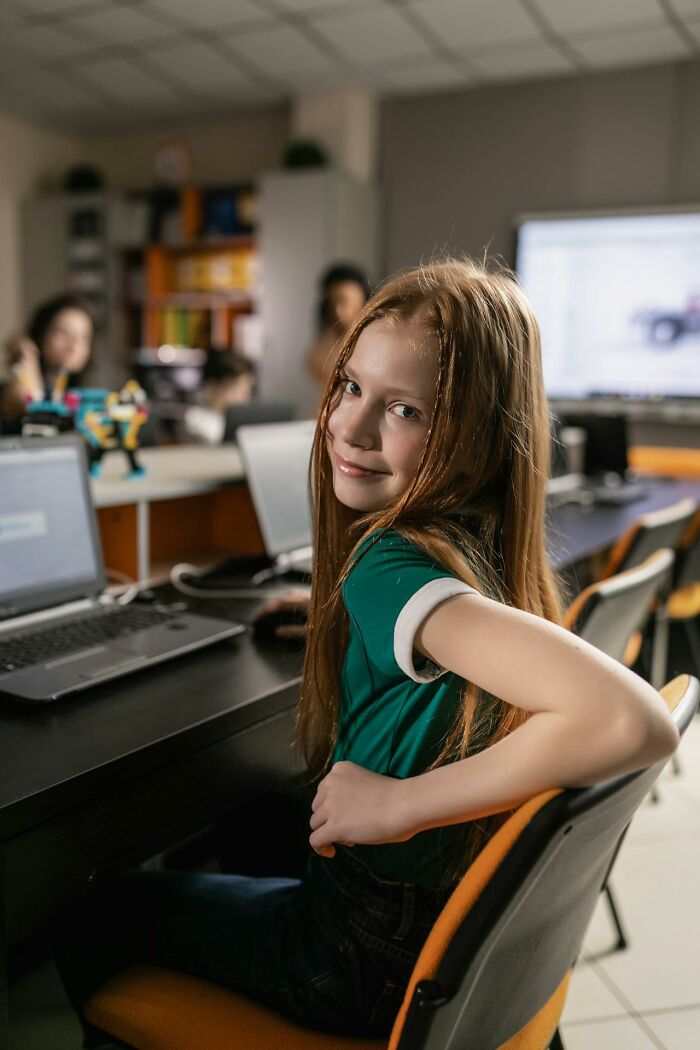 Young girl sitting at a desk in a classroom with laptops, capturing an embarrassing moment that is hilarious to remember.