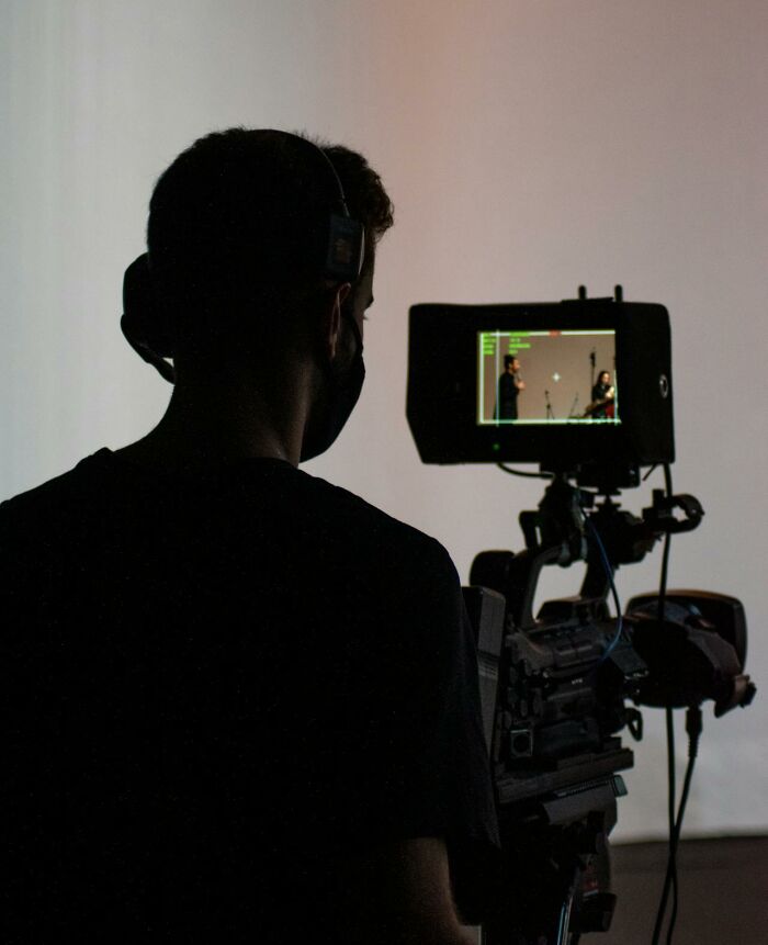 Person wearing headphones filming a true crime interview scene with professional camera equipment in a dimly lit room.