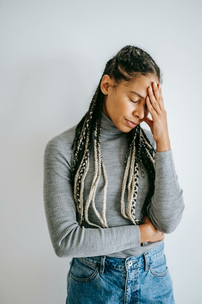Young woman with braided hair wearing a gray turtleneck showing emotional pain reflecting broken trust by close friends.