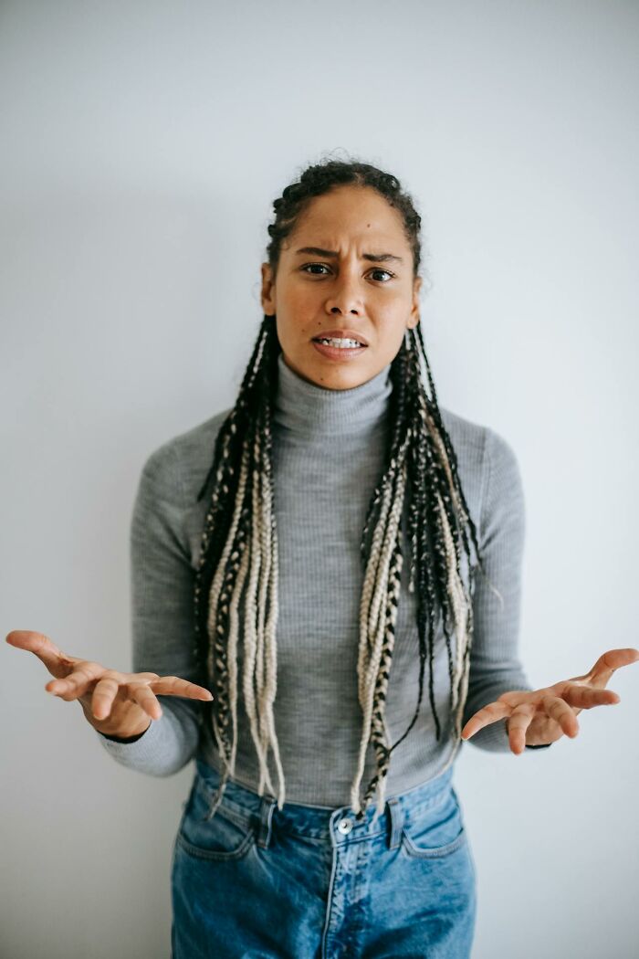 Woman with braids in gray turtleneck and jeans showing confused expression, illustrating signs someone is having an affair.