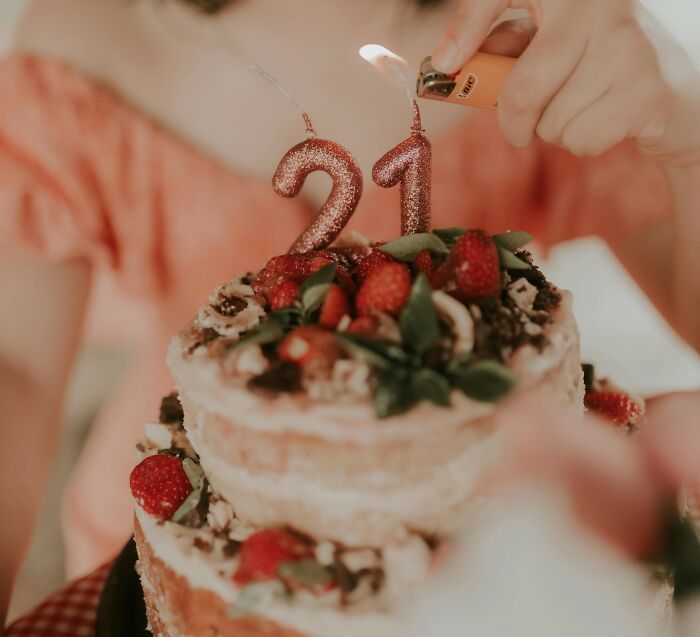 Person lighting number 21 candles on a strawberry cake, illustrating painful table for two moment turned table for one.