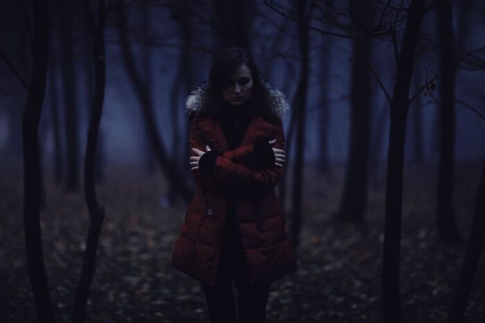 Woman in a red coat standing alone in a dark, eerie forest at night representing true crime fans' mysterious appeal.