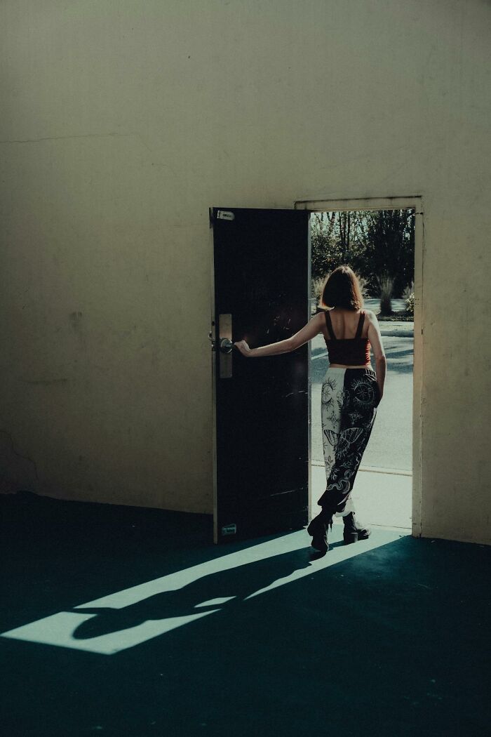 Woman walking out of a dark room into sunlight, symbolizing heartbreak and broken trust by close friends.