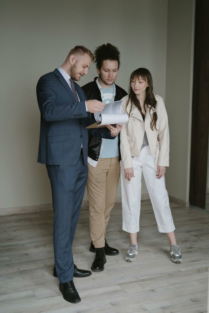 Three people, two men and a woman, reviewing documents together indoors, highlighting subtle sexist dynamics in conversation.