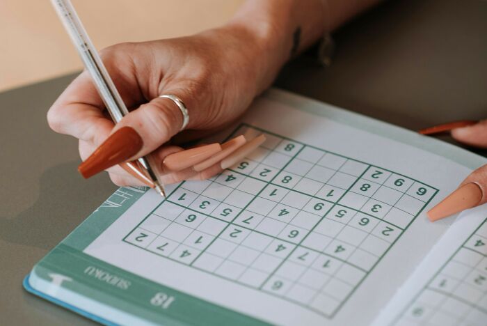 Person solving a sudoku puzzle in a book, focusing on filling numbers in challenging brain-racking sudoku grids.