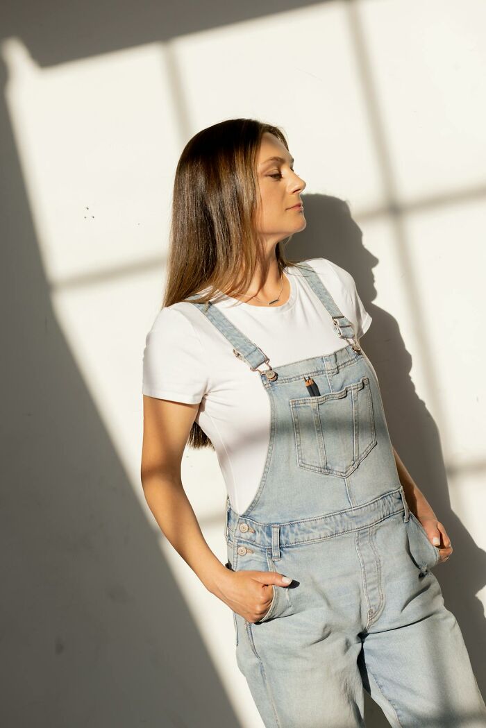 Young woman in denim overalls and white shirt standing in sunlight, illustrating subtle everyday sexism against men.