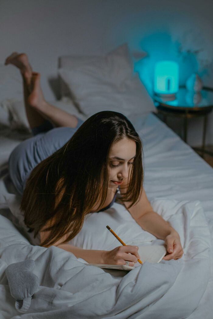 Young woman writing notes on a bed at night, reflecting on online dating advice and personal experiences.