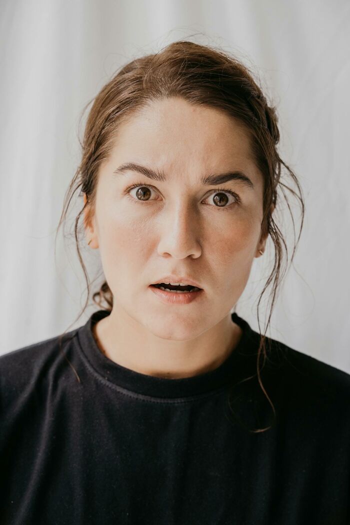 Woman with shocked expression reacting to one of the worst and craziest funeral stories in an indoor setting.