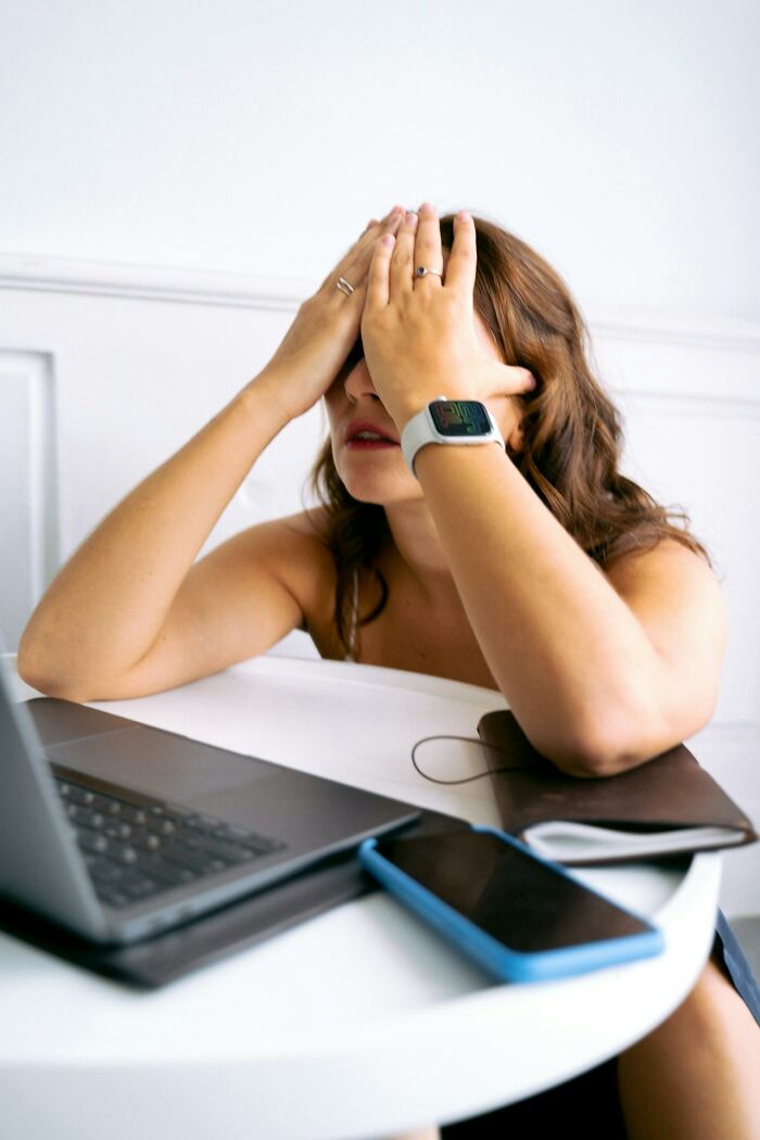 Woman with smartwatch sitting at table with laptop and phone, showing frustration related to subtle sexist experiences.