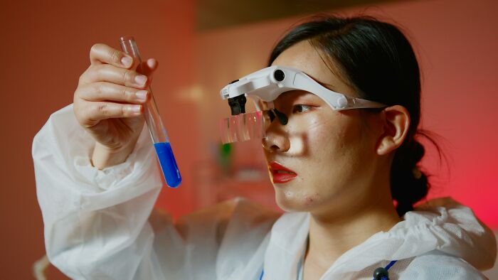 Scientist in protective gear examining a test tube with blue liquid, highlighting people share potentially dangerous situations.
