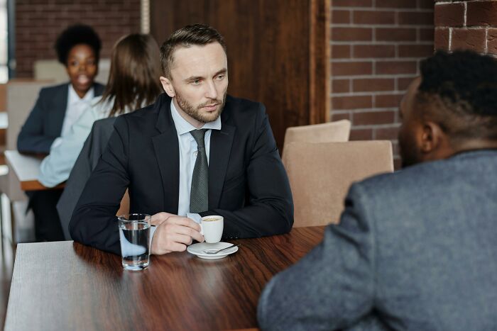 Two men in business attire having a serious conversation at a wooden table in a professional setting.