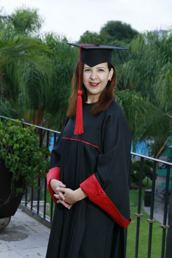Woman in black and red graduation gown smiling outdoors, illustrating topics related to sexism and gender inequality.