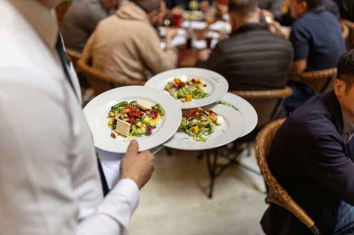 Waiter serving three plates of salad to a group of people dining, capturing a moment of social embarrassment and funny stories.