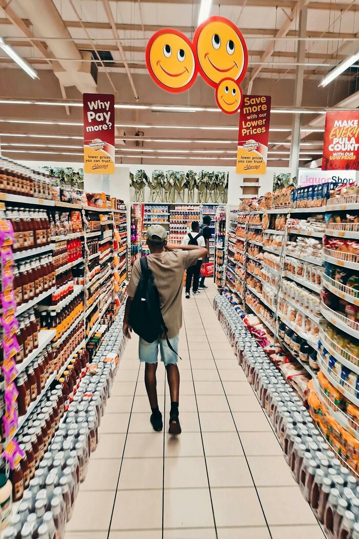 Man shopping in a grocery store aisle with products on shelves, illustrating subtle everyday sexism and height barriers.