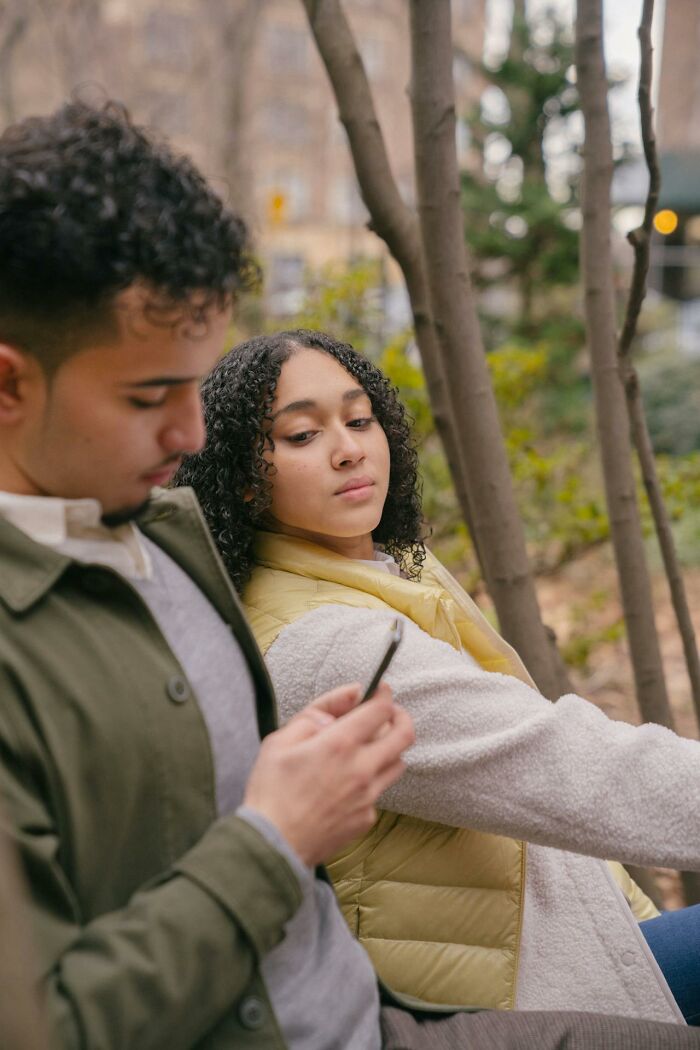 Young woman looking suspiciously at man using phone outdoors, illustrating first signs that scream someone is having an affair.