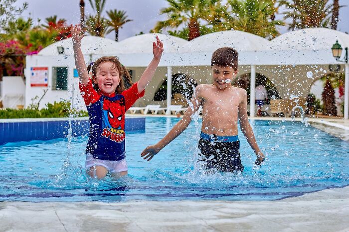 Two young boys splashing water and having fun in a pool, capturing hilarious moments of playful embarrassment.