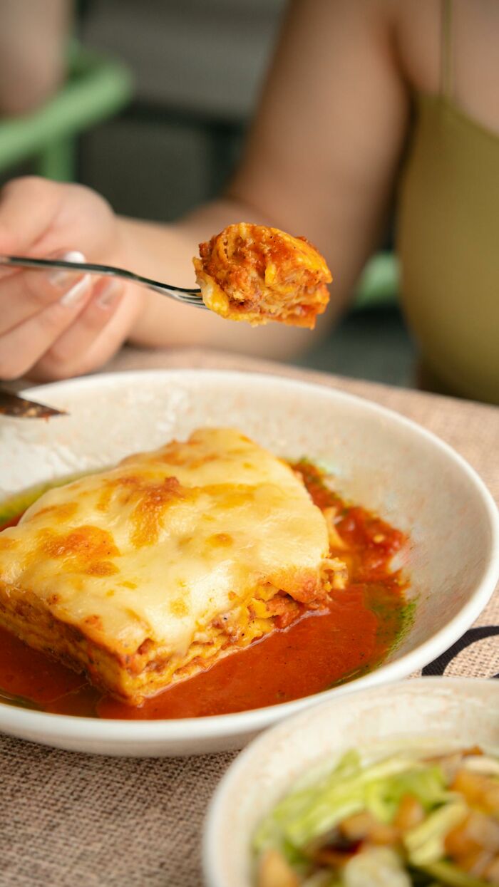 Person holding a fork with lasagna, close-up of cheesy lasagna in a bowl, depicting secrets people are hiding from their partners.