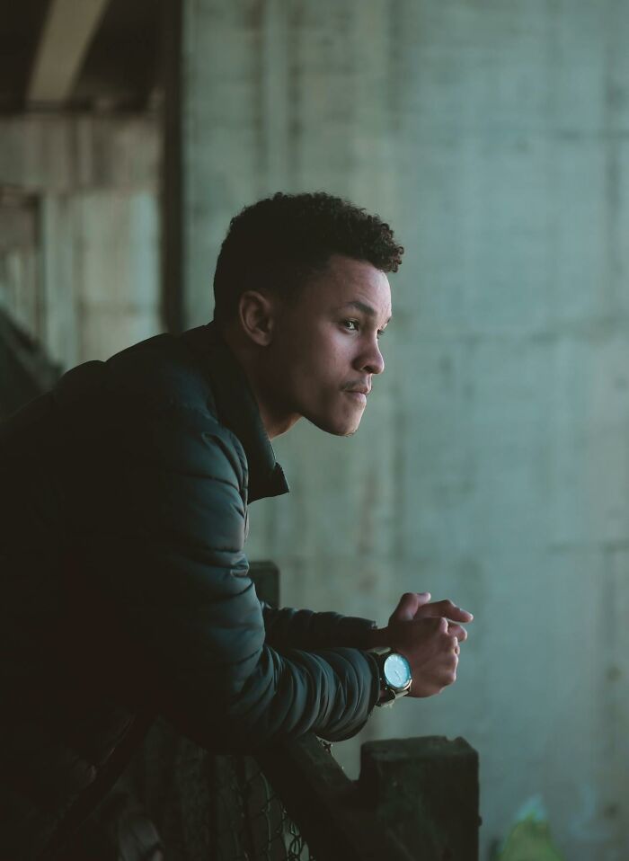 Young man in a dark jacket leaning on a railing, looking thoughtfully, representing online dating experience advice.