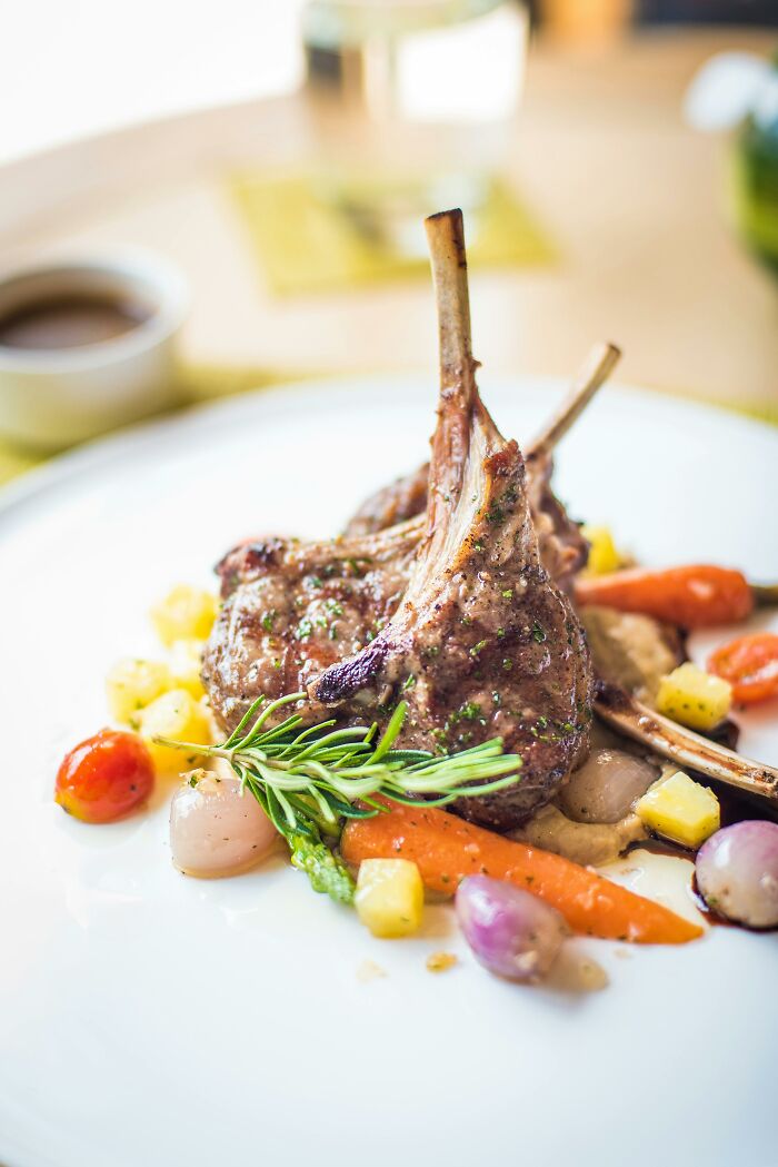 Grilled lamb chops with assorted vegetables on a white plate, highlighting uncommon popular foods in countries tourists mention.