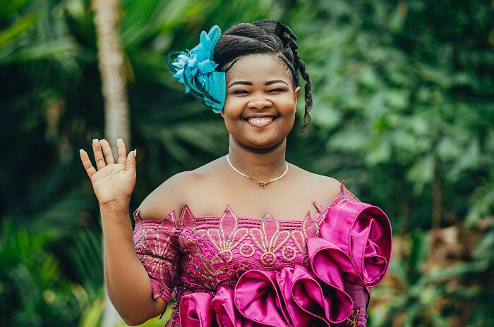 Smiling woman in vibrant traditional dress waving hand outdoors, representing foreign greetings and farewells for language geniuses.