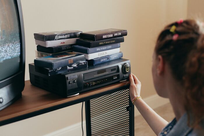 Person loading VHS tape into player with stack of VHS movies nearby, evoking 1980s movie expert nostalgia. Person loading VHS tape into player with stack of VHS movies nearby, evoking 1980s movie expert nostalgia.