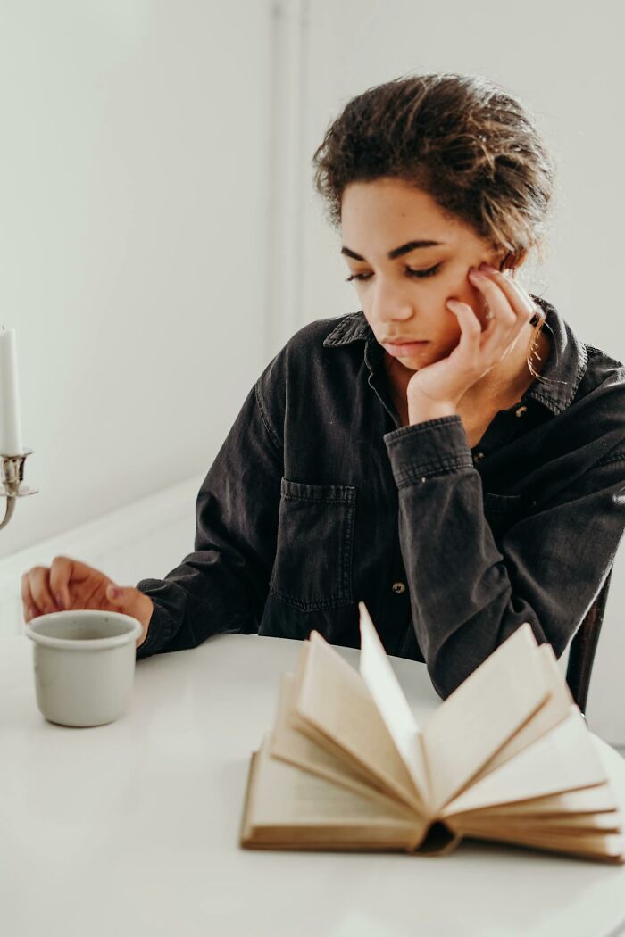Young woman looking thoughtful while reading a book and holding a cup, reflecting on signs someone is having an affair.