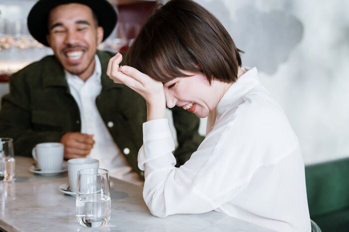 Two people laughing together at a café table, illustrating casual social interaction and subtle everyday sexism.