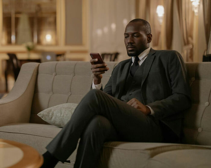 Man in a dark suit sitting on a couch, looking thoughtfully at his phone, symbolizing spouses changing after the wedding.