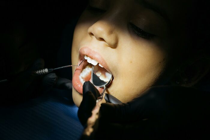 Close-up of an unvaccinated healthcare worker examining a patient's teeth using dental tools in a dim setting.