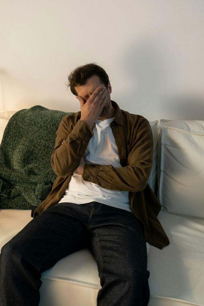Man sitting on a couch covering his face, illustrating frustration related to online dating experience advice.