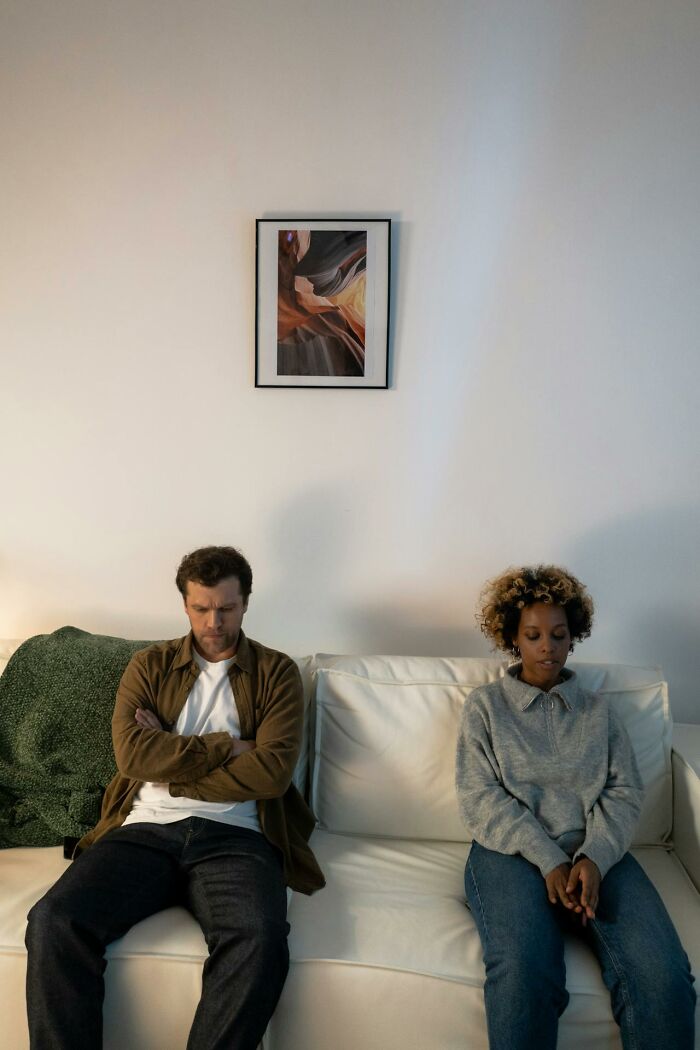 A couple sitting apart on a couch looking upset, representing first signs someone is having an affair.