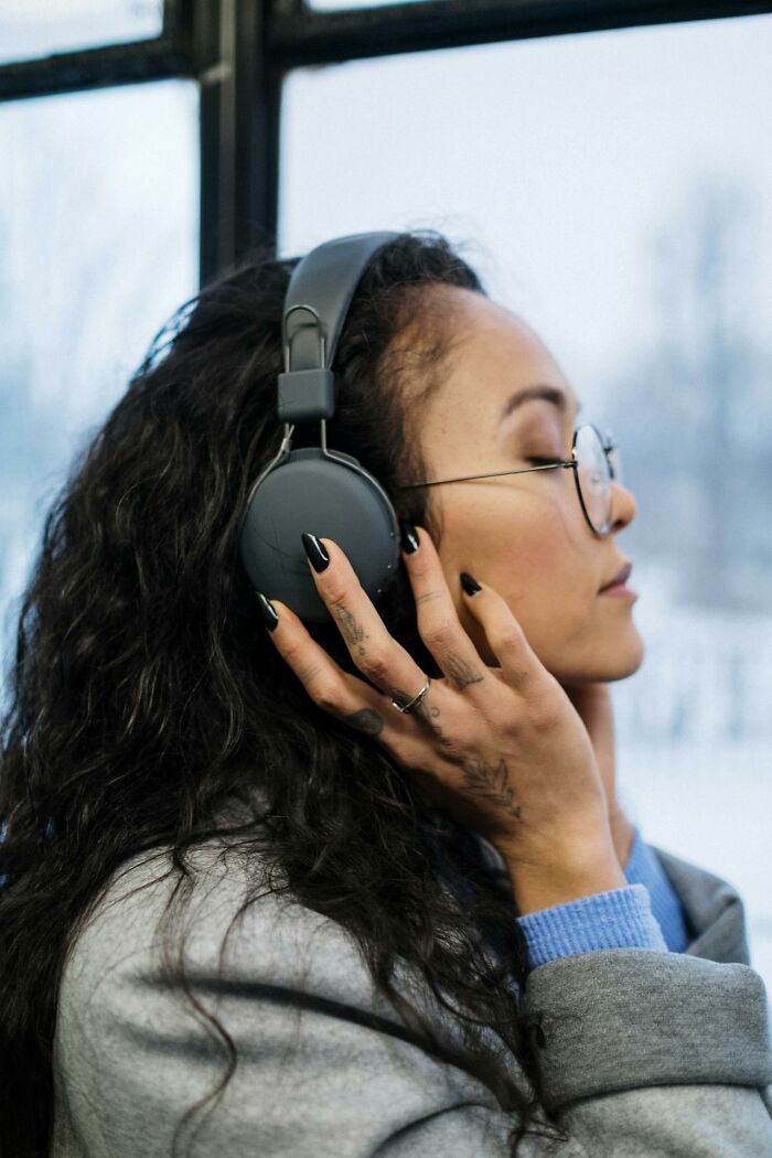 Young woman with headphones on, eyes closed, enjoying music while reflecting on secrets people hide from partners.