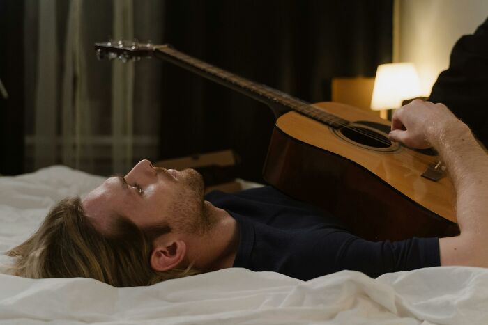 Young man lying on bed playing guitar, reflecting on chaotic and dramatic breakup stories and emotions.