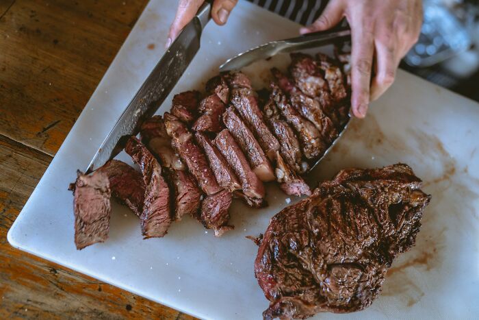 Close-up of a waiter slicing grilled steak on a cutting board, illustrating a painful table for two moment ending table for one.