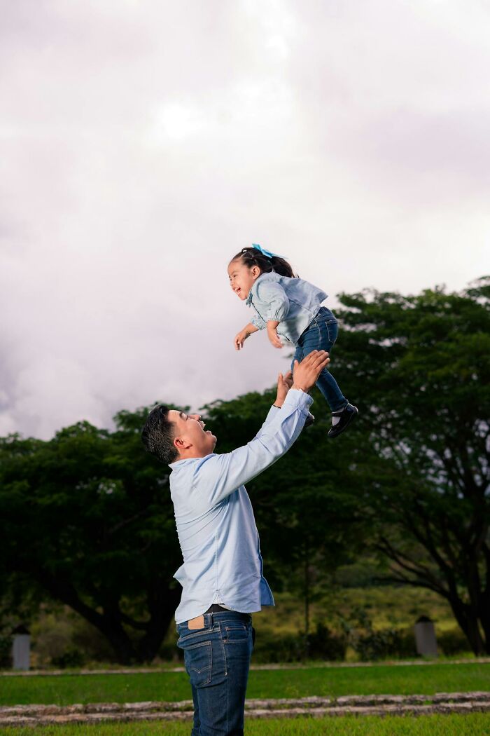 Man playing outdoors lifting a smiling child in the air, highlighting everyday sexism and gender roles.