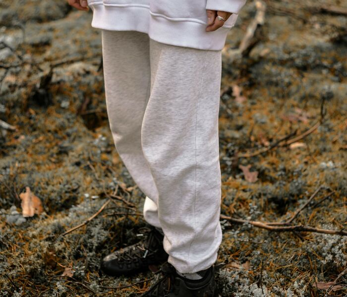 Person wearing white sweatpants and black shoes standing outdoors on mossy ground, symbolizing painful table for two moments.