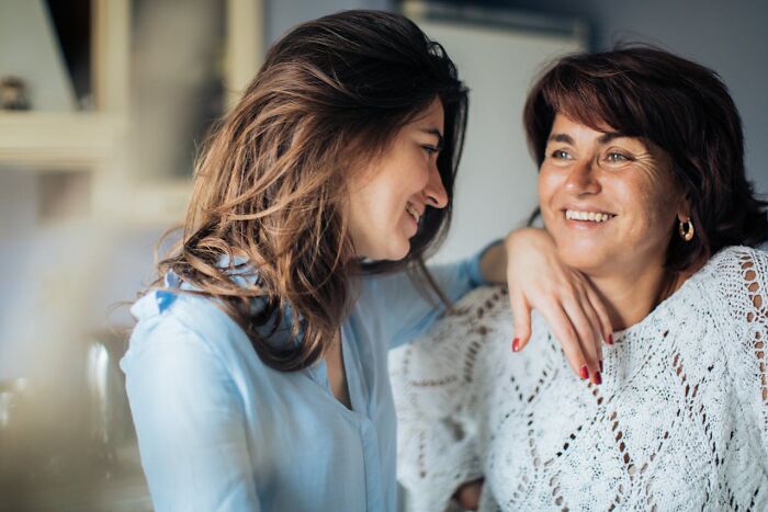Two women smiling and talking closely, illustrating secrets people are hiding from their partners in a warm setting.