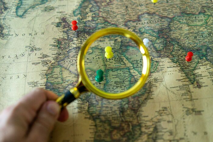 Magnifying glass focusing on Africa with colorful pins on a vintage map for geography expert challenge.