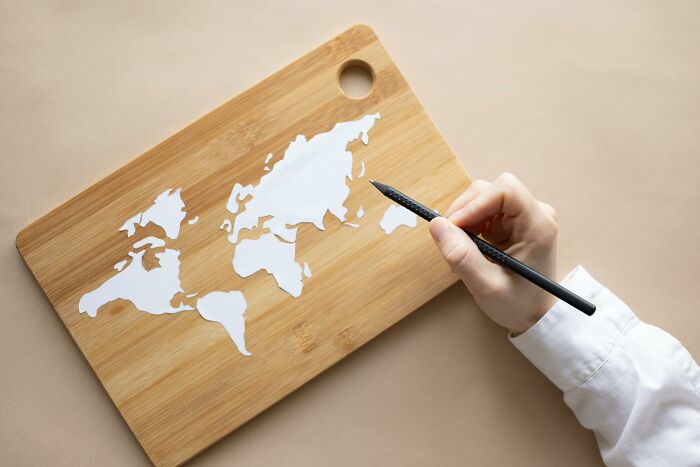 Hand holding pen near world map on wooden board representing visual geography quiz concept.