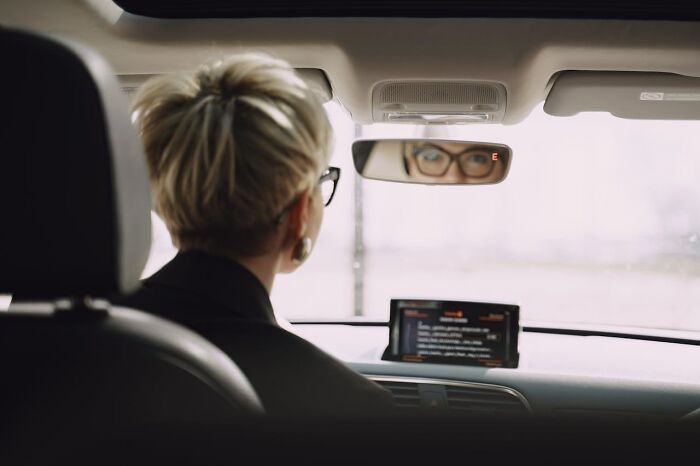 Person with glasses looking in a car rearview mirror, symbolizing karma striking with zero mercy concept.