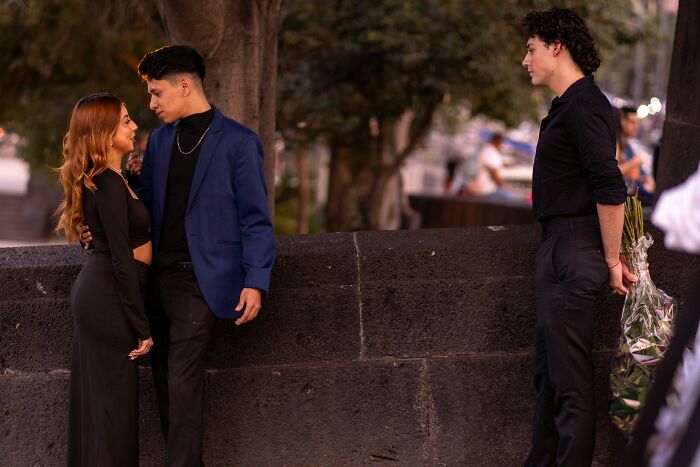 A tense breakup moment with a couple confronting each other while a third person waits holding flowers.
