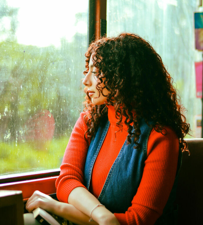 Young woman with curly hair looking thoughtfully out a window, reflecting on unexplainable creepy experiences.