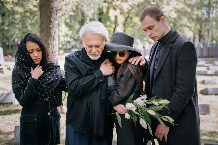 Four mourners at a gravesite showing grief and support, illustrating emotions often explored by true crime fans.