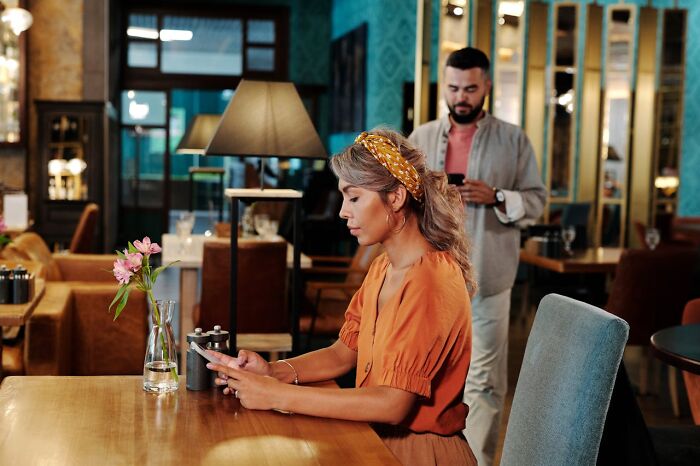 Woman and man using smartphones in a cozy restaurant, representing online dating advice from experienced people.