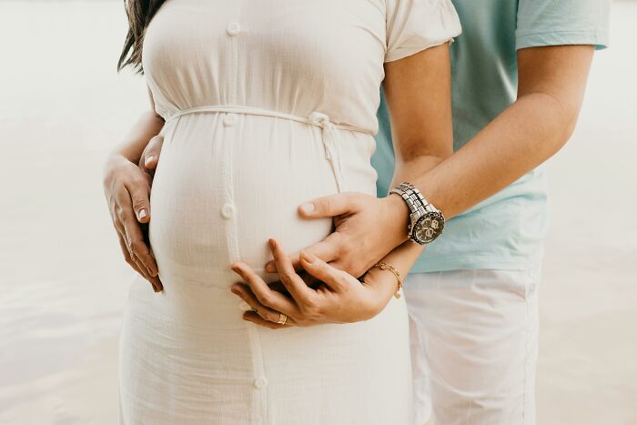 Pregnant woman in white dress with partner holding her belly, illustrating chaotic and dramatic breakup stories.