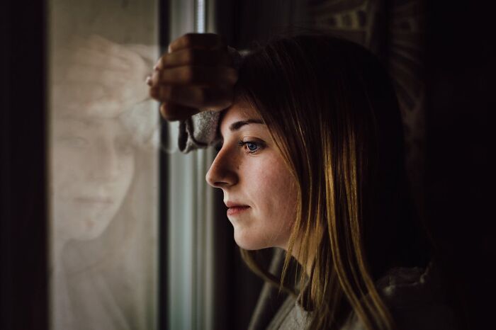 Young woman looking thoughtfully out a window, illustrating online dating experience and advice reflection.