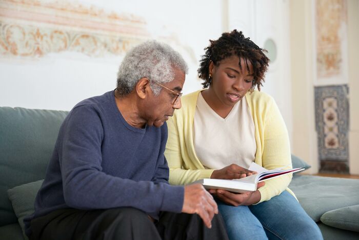 An unvaccinated healthcare worker and an elderly man reviewing medical information together on a couch at home.