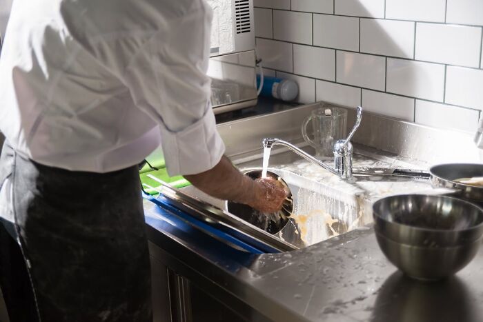 Man washing dishes in a kitchen sink highlighting everyday sexist expectations and gender roles for men in household chores
