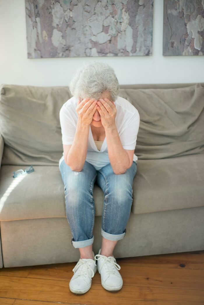Elderly woman sitting on a couch covering her face, feeling heartbreak and betrayal from close friends breaking trust forever.