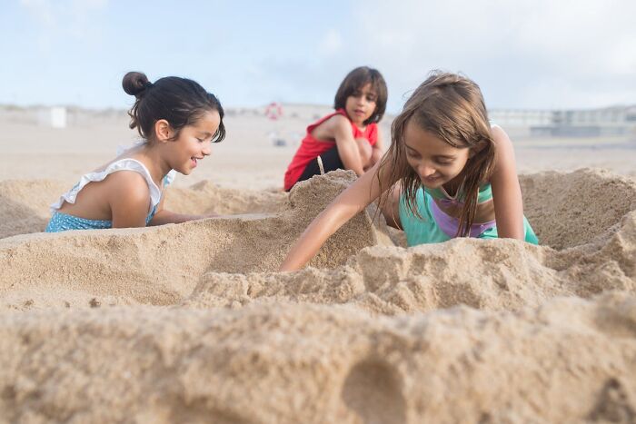 Niños jugando en la playa mientras están enterrados en la arena, mostrando momentos de karma instantánea y diversión.